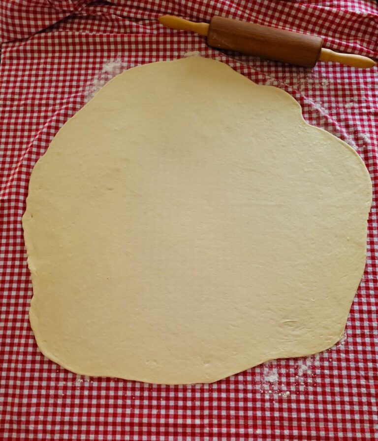 Ausgerollter Teig auf einer roten Tischdecke.