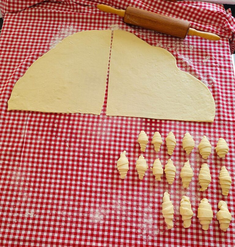 Teig und mehrere Brötchen auf einer roten Tischdecke.